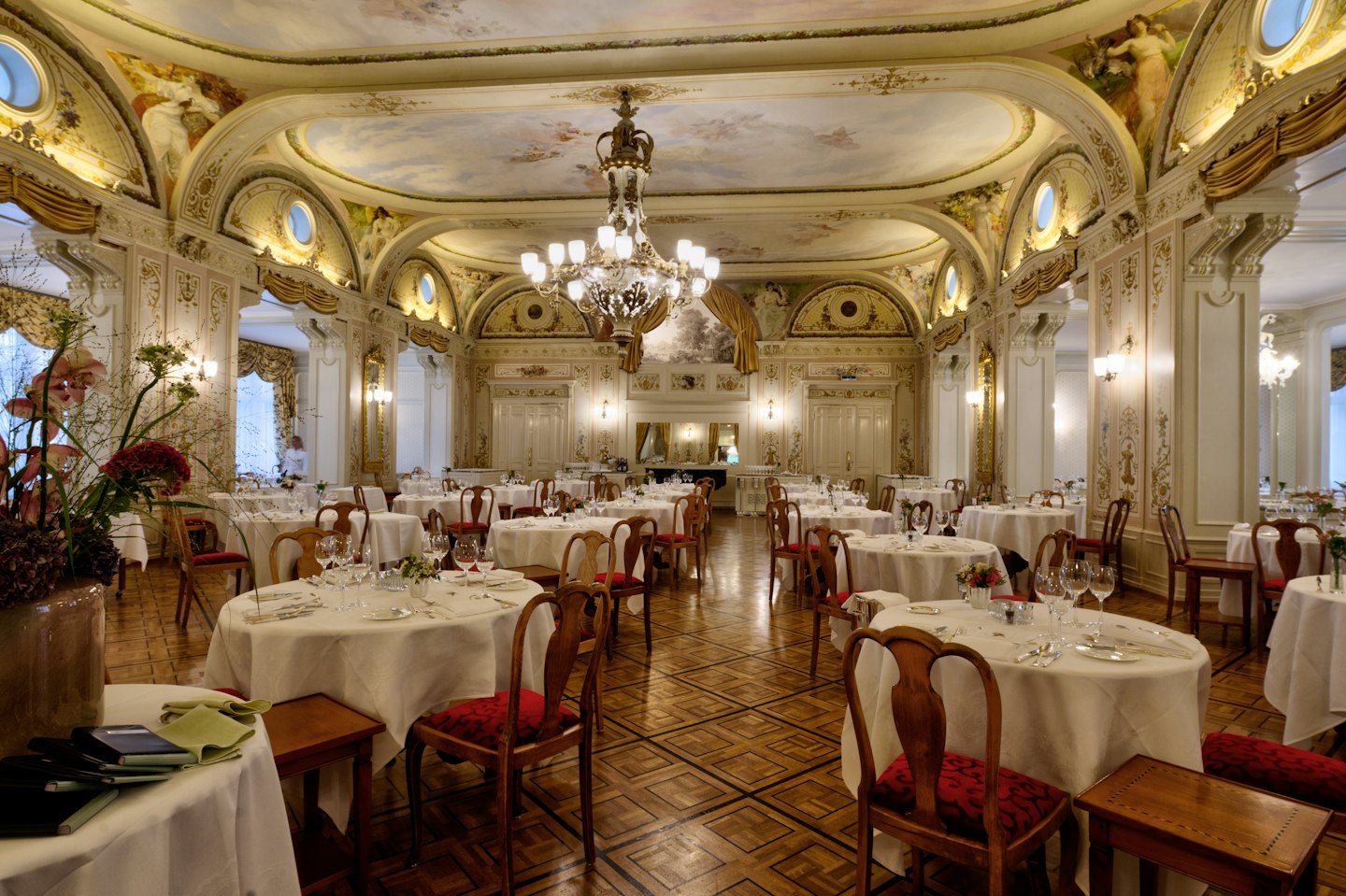 Elegancka sala balowa z nakrytymi stołami pod kryształowym żyrandolem.