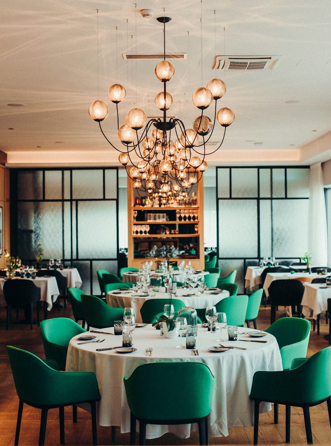 Elegancka sala restauracyjna z okrągłymi stołami i zielonymi krzesłami.