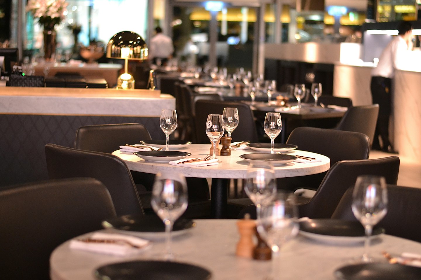 Elegancka sala restauracyjna z marmurowymi stołami i skórzanymi krzesłami.